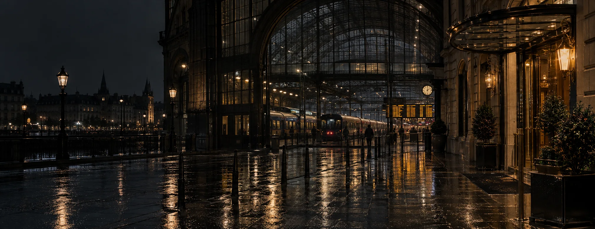 Rain-soaked stone outside a European railway station, with a warmly lit hotel entrance nearby